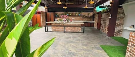 An outdoor kitchen area with a stone floor, a central island, and hanging pendant lights.