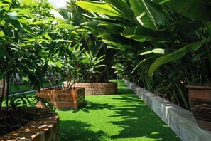 Un jardín con césped artificial, macetas de ladrillo y diversas plantas verdes.