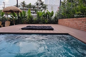 A swimming pool with a wooden deck, a black lounge chair, and tropical plants.