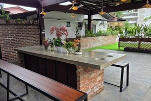 An outdoor bar area with a concrete countertop, a wooden bench, and potted plants.