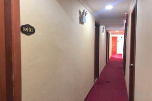Un couloir d’hôtel avec un tapis rouge, une enseigne portant le numéro 8401 et une porte au bout.