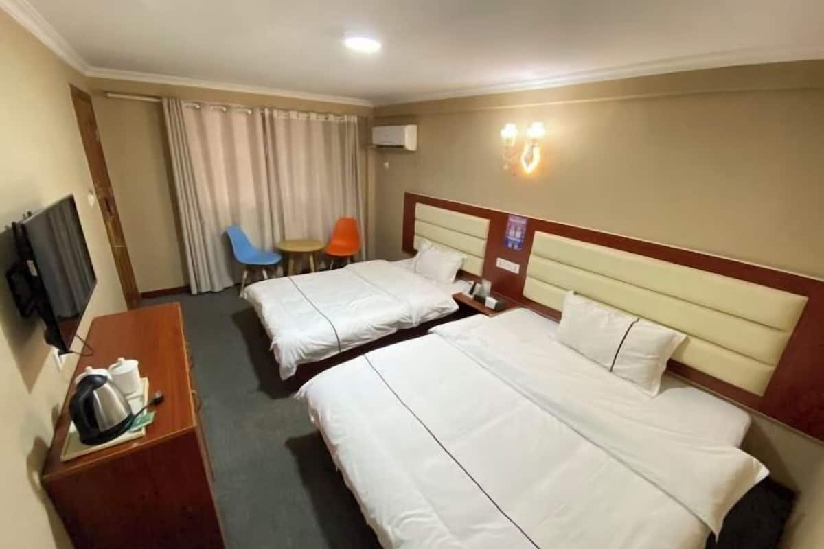 Ein Hotelzimmer mit zwei Betten, einem Schreibtisch mit Wasserkocher, einem Fernseher und einem Sessel.