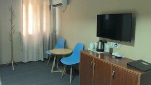 Une chambre d’hôtel équipée d’une télévision, d’une armoire en bois, d’une table avec des chaises et d’un appareil de climatisation.