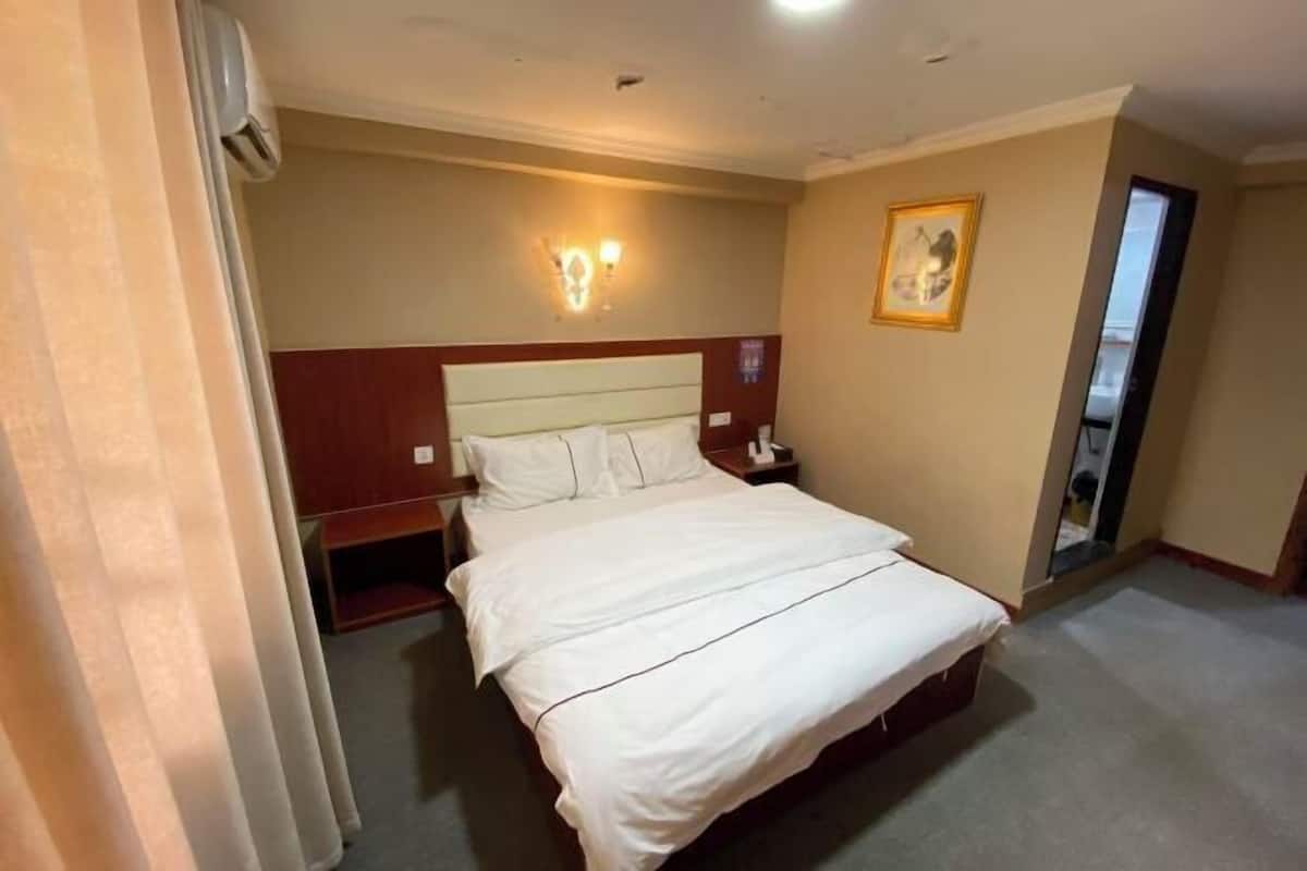 Ein Hotelzimmer mit einem Bett, einem Nachttisch, einer Wandleuchte und einem gerahmten Bild.