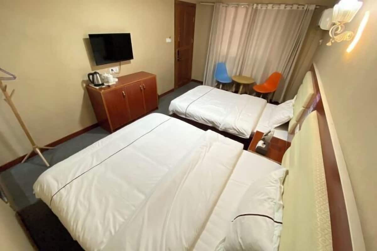 Ein Hotelzimmer mit zwei Betten, einem Fernseher, einem Schrank und einem kleinen Tisch mit Stühlen.