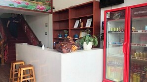 Un espace d’accueil comprenant un comptoir, des tabourets en bois, un réfrigérateur rouge et un escalier.