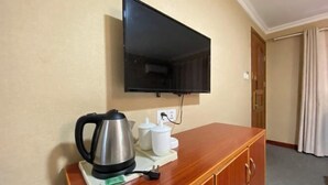 Une chambre d’hôtel équipée d’un téléviseur à écran plat fixé au mur, d’un meuble en bois contenant une bouilloire et des tasses, et d’une porte donnant sur une autre pièce.