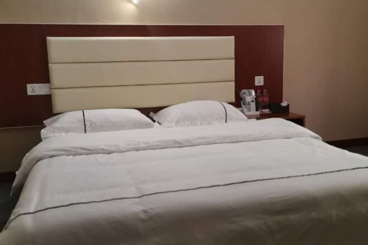 Ein Hotelzimmer mit einem großen Bett, einem Kopfteil, einem Nachttisch und einer Steckdose.