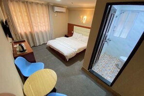 Une chambre d’hôtel comprenant un lit, un bureau, une chaise, une petite table et un espace douche.