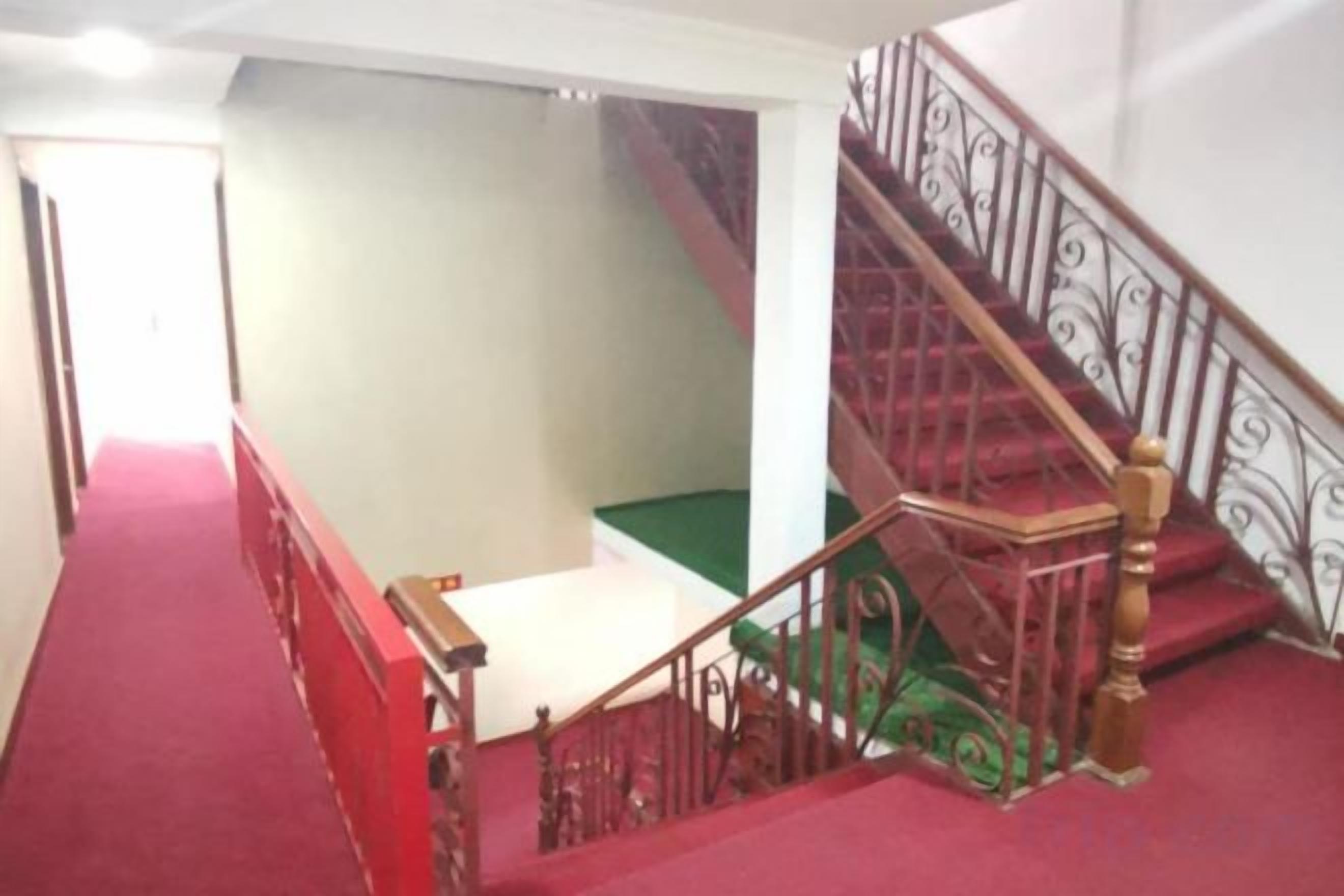 Un escalier recouvert d’une moquette rouge, avec un palier vert et une rampe en métal.