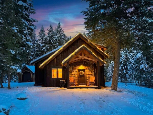 A wooden cabin with a porch, surrounded by snow-covered trees.