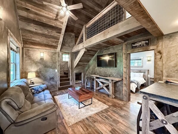 A rustic interior with a wooden ceiling, a staircase, a sofa, a coffee table, and a TV mounted on the wall. - The Glacier by Bison Ridge Retreat (Whitefish)
