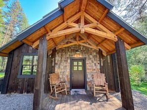 A rustic wooden cabin with a porch, a door, and two rocking chairs.