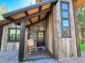 Une cabane rustique avec un mur en pierre, un revêtement extérieur en bois et une véranda dotée d’un fauteuil à bascule.