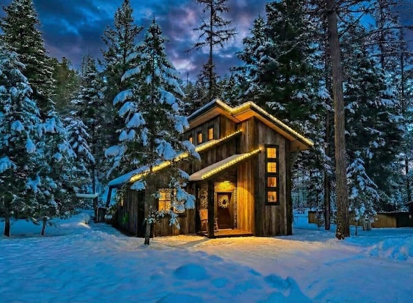 Une cabane en bois dotée d’un porche, entourée d’arbres couverts de neige.