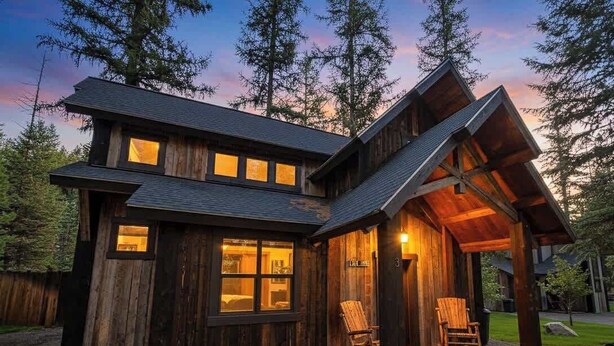 Un chalet rustique doté d’une grande véranda, d’une façade en bois et de nombreuses fenêtres.