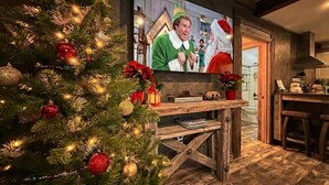 Un salon chaleureux avec un sapin de Noël décoré, un meuble de rangement en bois et un téléviseur diffusant une scène festive.