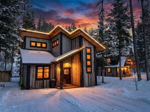 Une cabane en bois dotée d’une grande véranda, de nombreuses fenêtres et surplombant un paysage enneigé.