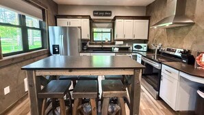 A modern kitchen with a central island, stainless steel appliances, and a view through the window. - The Solace by Bison Ridge Retreat (Whitefish)