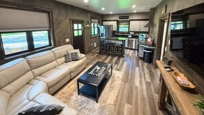 A modern living room with a sofa, coffee table, and kitchen area with bar stools. - The Solace by Bison Ridge Retreat (Whitefish)