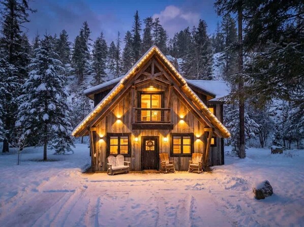 A log cabin with a balcony, surrounded by snow-covered trees.
