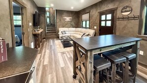 A modern kitchen with a central island, a dining area with a table and chairs, and a living room with a sofa. - The Solace by Bison Ridge Retreat (Whitefish)