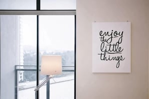 Una habitación con un gran ventanal, una lámpara y una cita inspiradora en la pared.