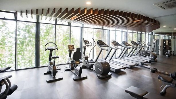 Une salle de sport équipée de tapis de course, de vélos d’appartement et d’appareils de musculation, dotée de grandes fenêtres et d’un design moderne au niveau du plafond.