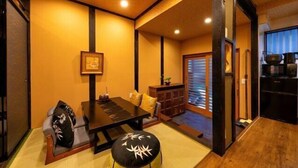 A traditional Japanese room with tatami flooring, a low table, cushions, a sliding door, and a kitchen area. - AOU･SEITOKKU (Osaka)
