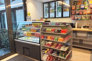 A refrigerated display case with various beverages, shelves stocked with snacks and packaged goods, and a view of the outside through large windows. - Ofton Elysium Soul Residence (Istanbul)