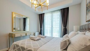 Una habitación de hotel moderna con una cama grande, una mesita de noche, un espejo y una ventana con cortinas.