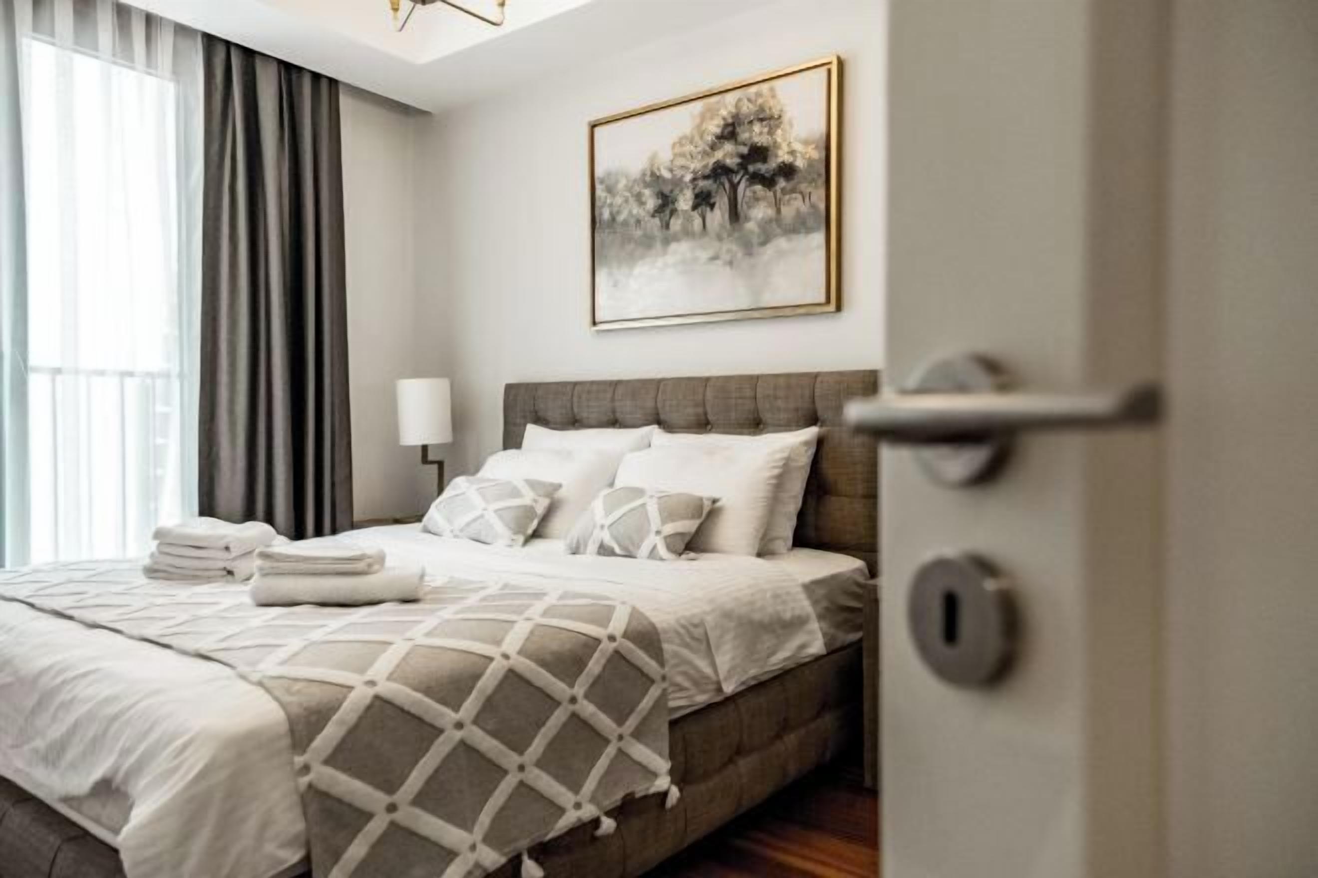 A neatly made bed with a geometric-patterned blanket, a bedside lamp, and a framed picture on the wall.