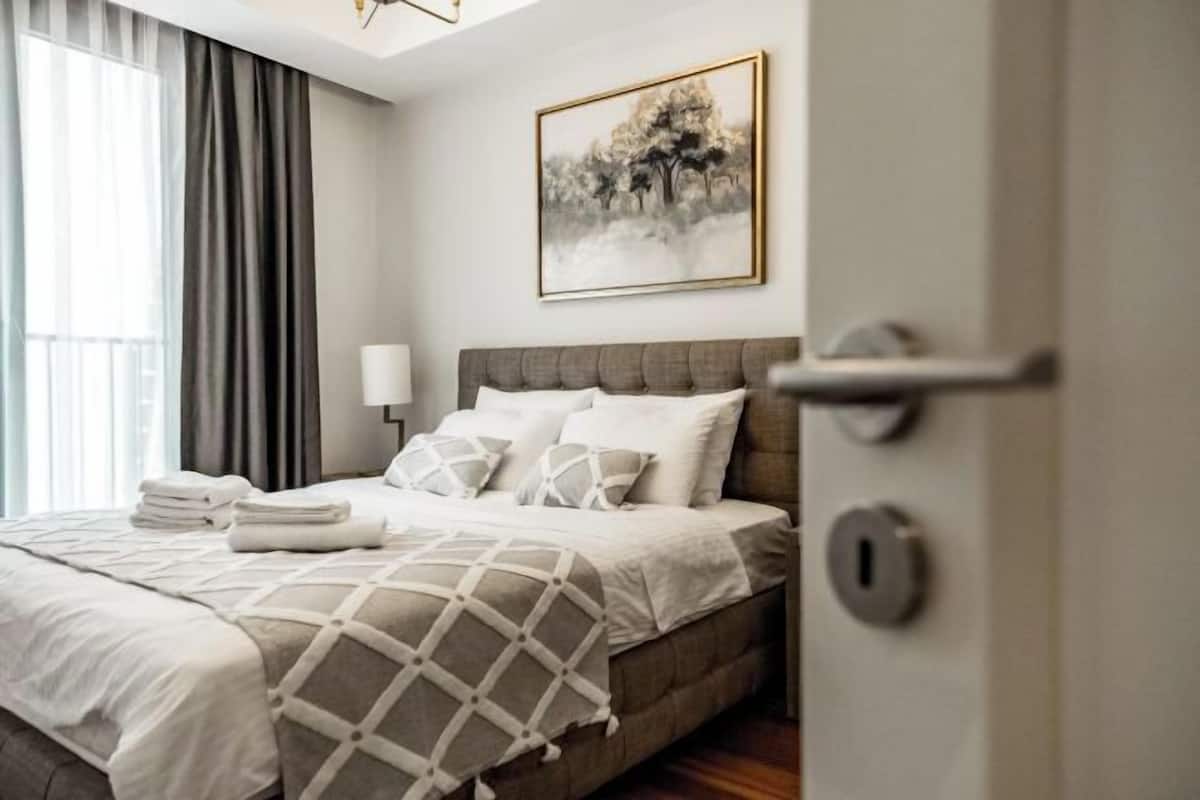 A neatly made bed with a geometric-patterned blanket, a bedside lamp, and a framed picture on the wall.