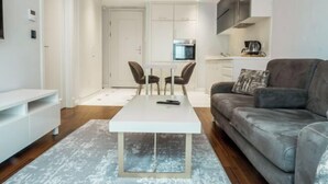 Una sala de estar moderna con un sofá gris, una mesa de centro blanca y un comedor con una mesa y sillas blancas.