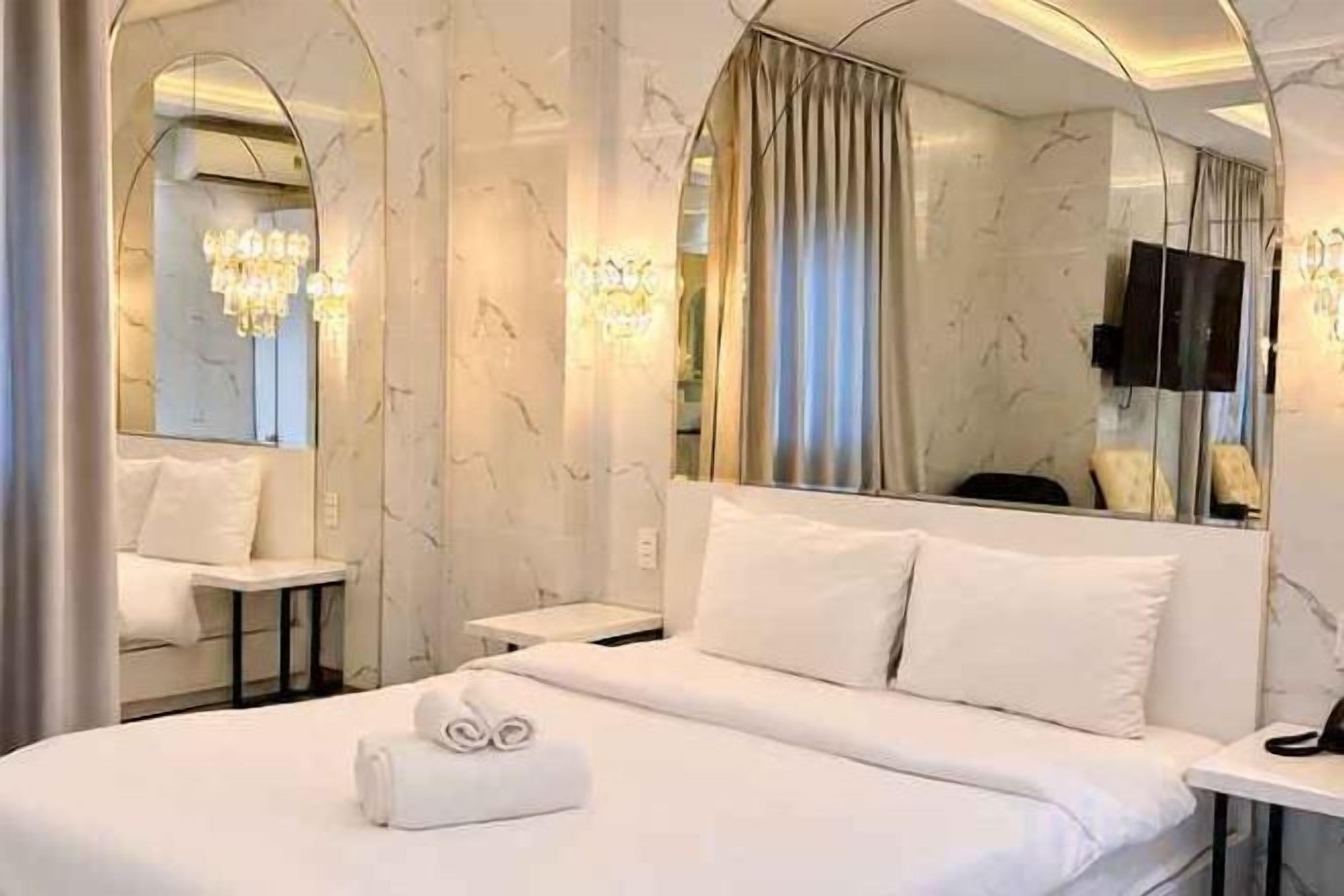 Une chambre d’hôtel avec un lit, une table de chevet, un miroir et un lustre.