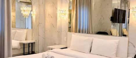 A hotel room with a bed, a bedside table, a mirror, and a chandelier.