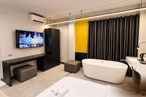 A modern hotel room with a flat-screen TV, a large white bathtub, a sofa, and a desk area. - A In Hotel Atistar (Ho Chi Minh City)