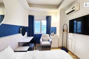 A hotel room with a bed, a desk, a chair, a small table, a mirror, a window with curtains, and an air conditioning unit. - A In Hotel Atistar (Ho Chi Minh City)