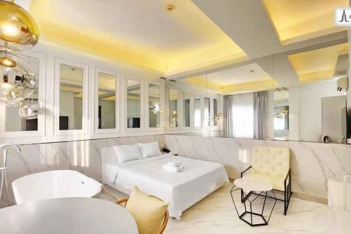 Une chambre d’hôtel moderne avec un grand lit, un coin salon, une baignoire et un grand miroir.