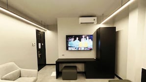 A modern living room with a flat-screen TV mounted on the wall, a black entertainment unit, and a seating area with a sofa and ottoman. - A In Hotel Atistar (Ho Chi Minh City)