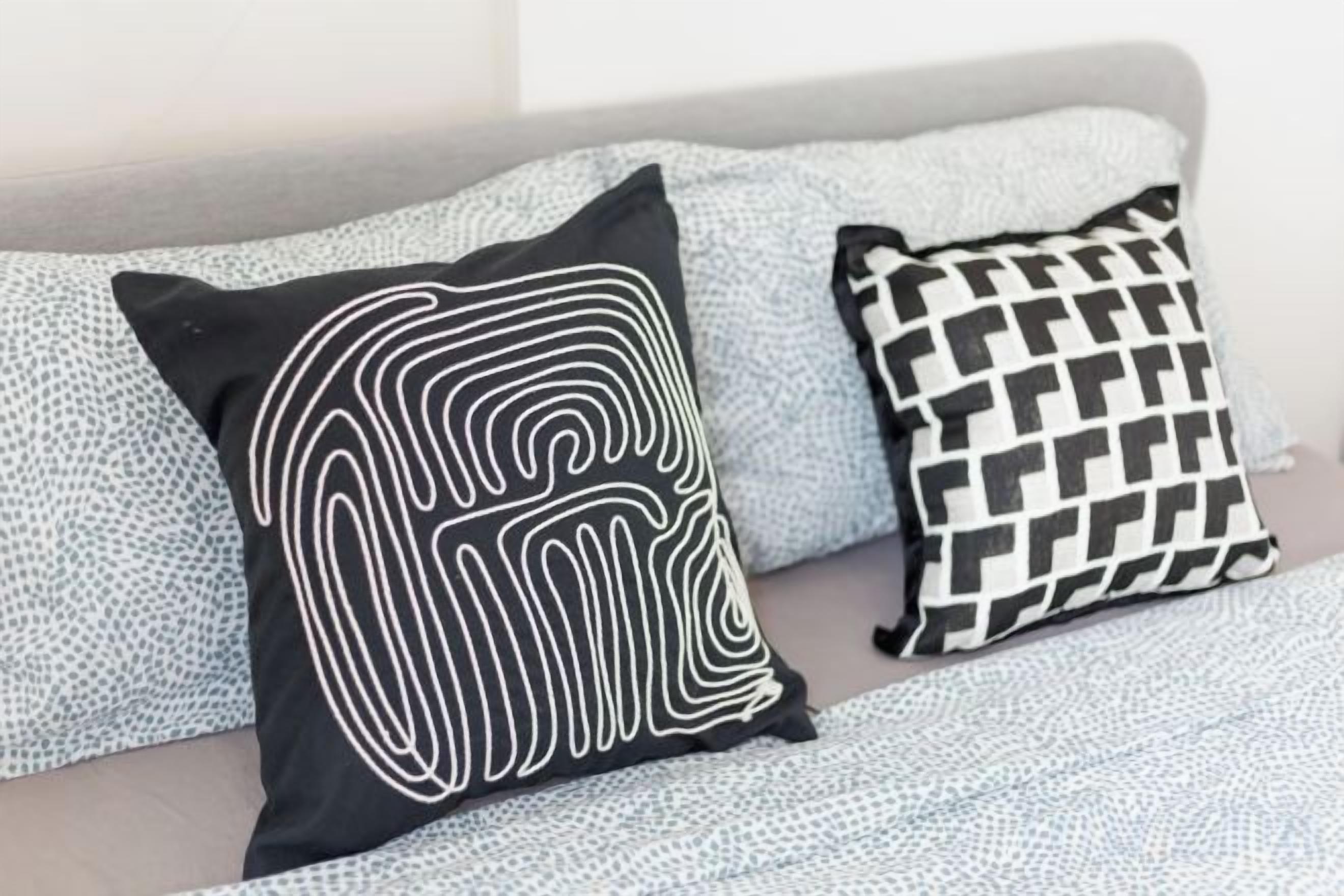 A bed with a grey headboard and two pillows with distinct patterns.