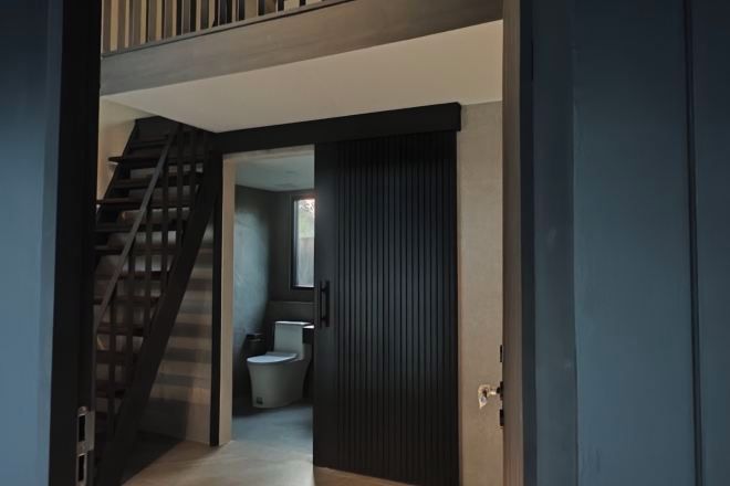 Een modern interieur met een trap naar een tweede verdieping, een donkere schuifdeur en een zichtbare badkamer met toilet en wastafel.