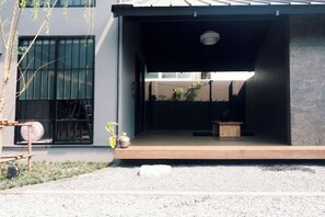 A modern building with a covered outdoor area, a wooden bench, and a small table. - Ojisan House (Chon Buri)