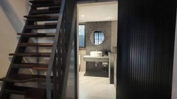 Een moderne badkamer met een ronde spiegel, een wastafel en een trap naar een ander gedeelte.