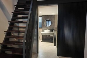 A modern bathroom with a round mirror, a sink, and a staircase leading to another area. - Ojisan House (Chon Buri)