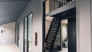 Un interior moderno con una escalera que sube a un nivel superior, ventanas amplias y un diseño minimalista.