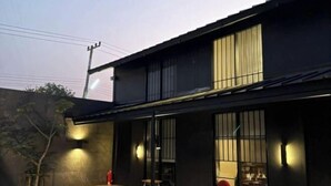 Un edificio moderno con fachada oscura, amplios ventanales y un pequeño espacio al aire libre con una mesa y sillas.