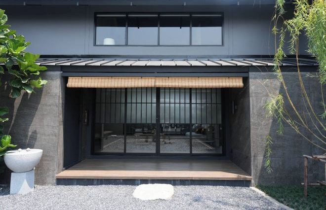 Een modern gebouw met een donkere gevel, grote ramen en een houten terras.