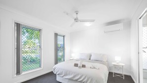 A modern bedroom with a large bed, a ceiling fan, and a window with a view of greenery. - Soothing 4-bedroom house with AC in Yarrabilba (Yarrabilba)