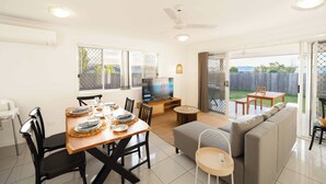 A spacious living area with a dining table set for four, a sofa, and a TV in the background. - Soothing 4-bedroom house with AC in Yarrabilba (Yarrabilba)
